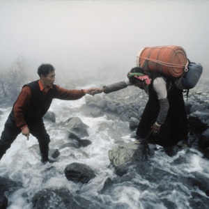 A villager from the Kham helps a woman carrying goods to cross a mountain torrent. (Tibet)